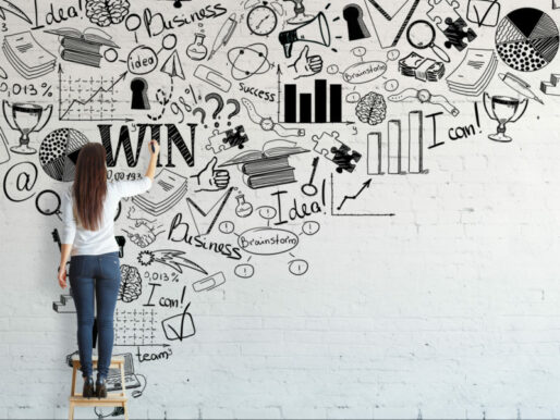 Rückansicht einer jungen Frau, die auf einem Hocker steht und eine kreative Geschäftsskizze auf einer Backsteinmauer zeichnet.