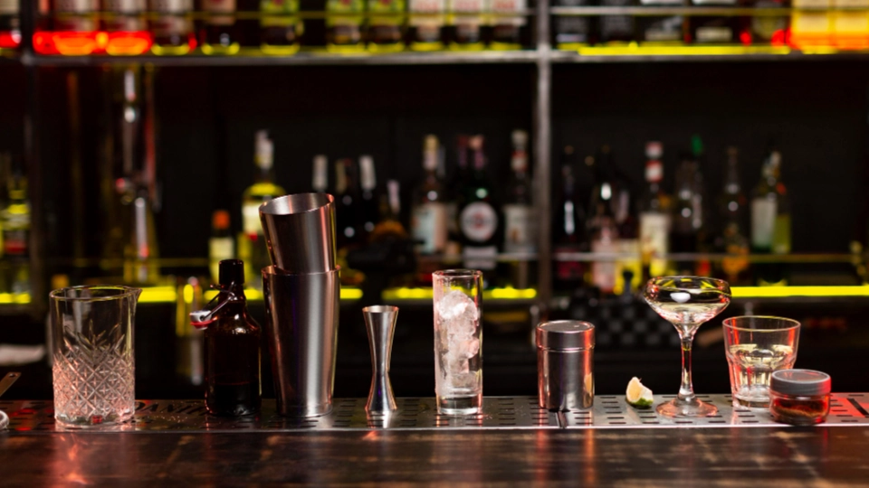 Cocktailgläser und Shaker auf einer Bar-Theke vor Flaschenregal
