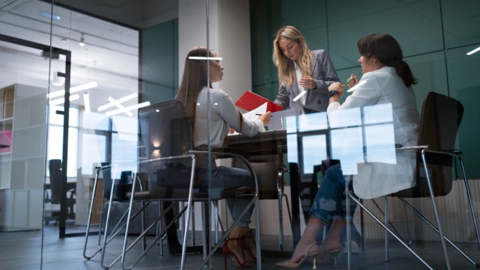 Drei Frauen im Büro-Meeting besprechen gemeinsam Unterlagen an einem Glastisch