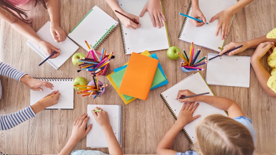 Vogelperspektive auf Kinder die gemeinsam an einem Tisch schreiben und zeichnen