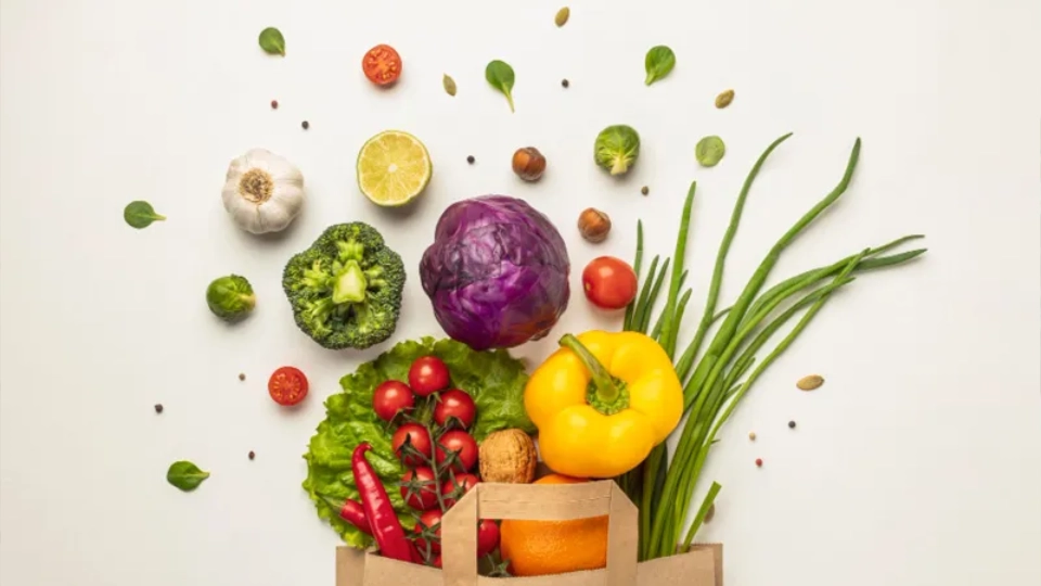 Frische Gemüse und Kräuter quellen aus einer Papiertüte auf weißem Hintergrund als Symbol für gesunde Ernährung