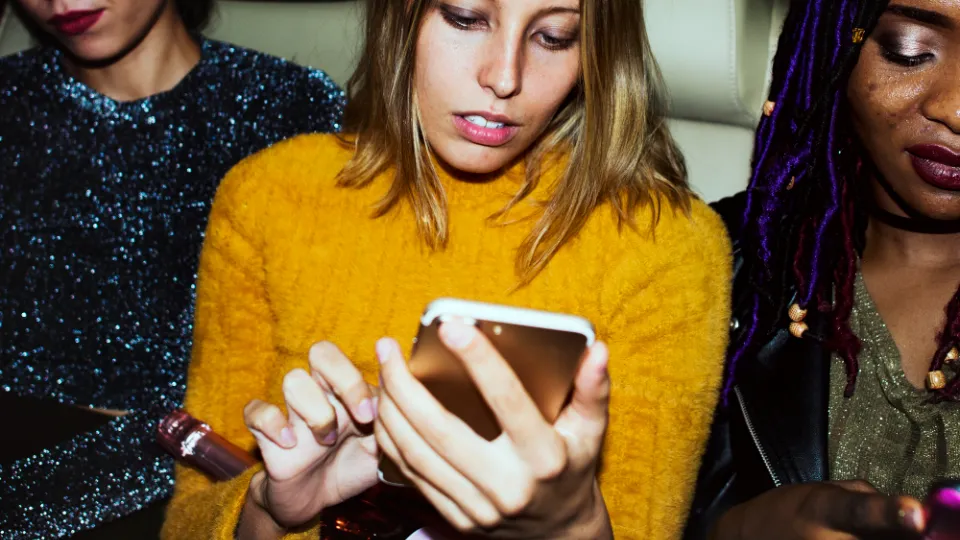 Drei junge Frauen schauen abends gemeinsam auf ein Smartphone