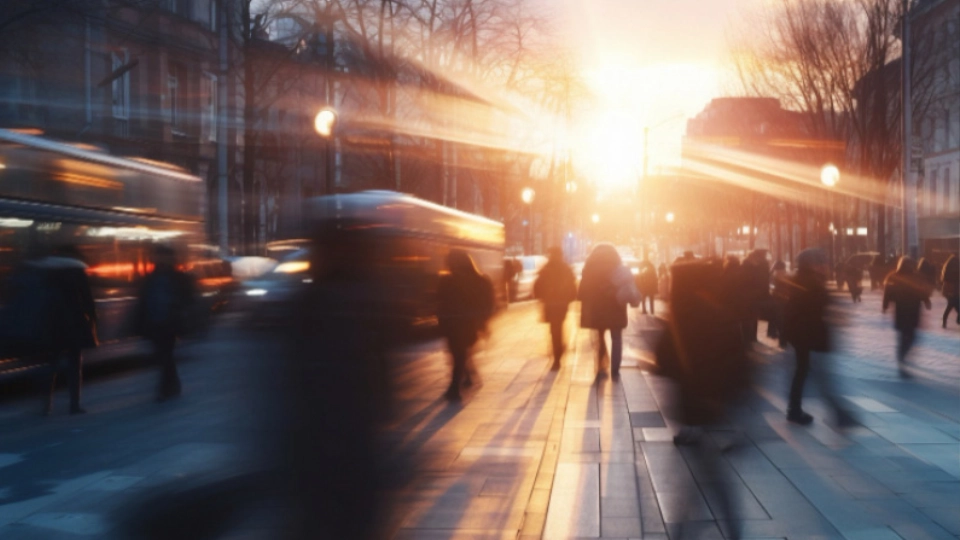 Verschwommene Langzeitbelichtung einer belebten Stadtstraße bei Sonnenuntergang mit Fußgängern und Bus