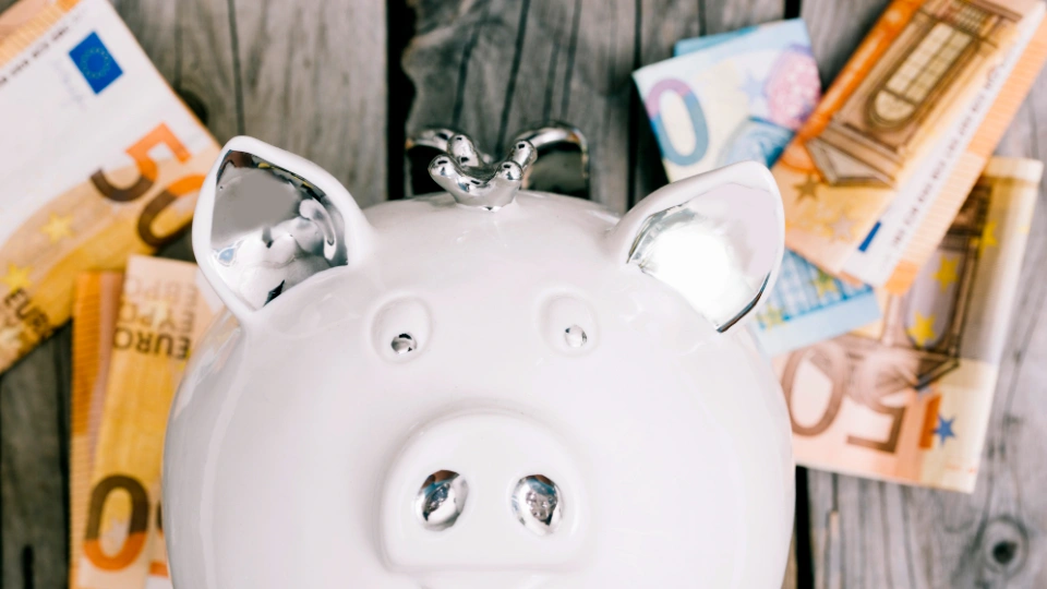 Weißes Sparschwein liegt auf dem Rücken umgeben von Euro-Geldscheinen als Symbol für Sparen und Finanzen