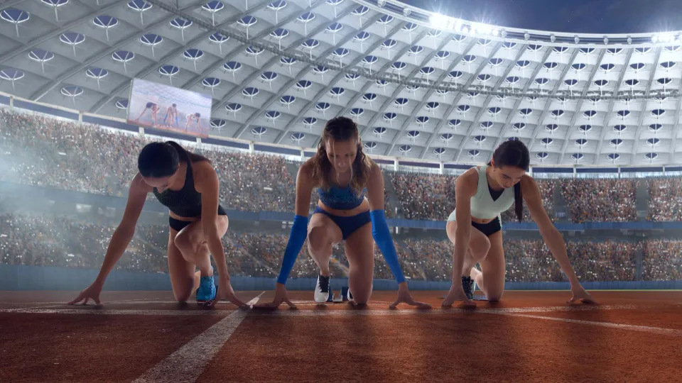 Drei Leichtathletinnen gehen in einer beleuchteten Stadionarena in die Startposition als Symbol für Sport und Wettkampf